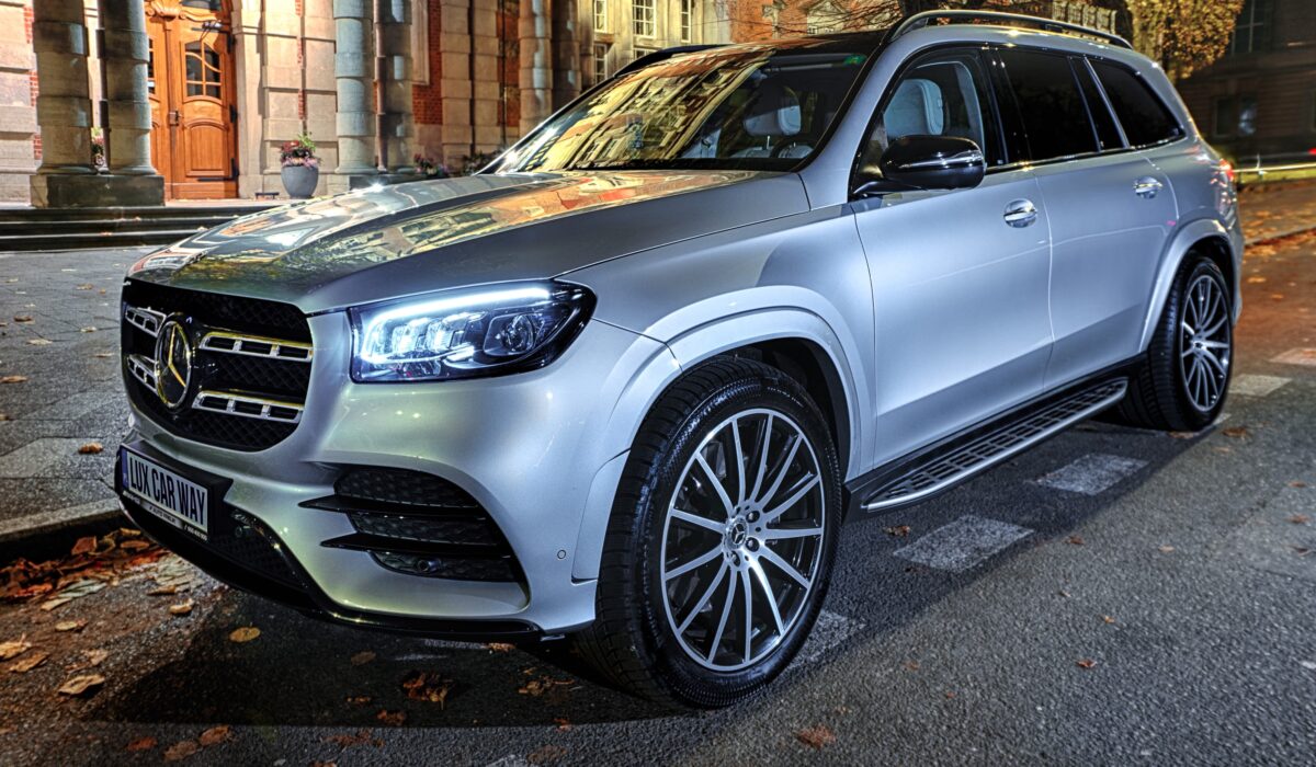 Srebrny Mercedes-Benz GLS zaparkowany przed zabytkowym budynkiem z cegły. SUV wyposażony w wieloramienne felgi aluminiowe i LED-owe reflektory. Jesienne liście widoczne na chodniku.